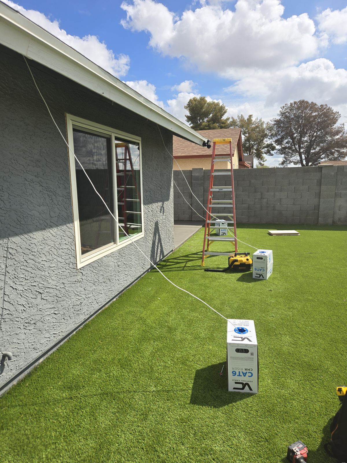 Ladder and tools set up for a camera install in a residential backyard