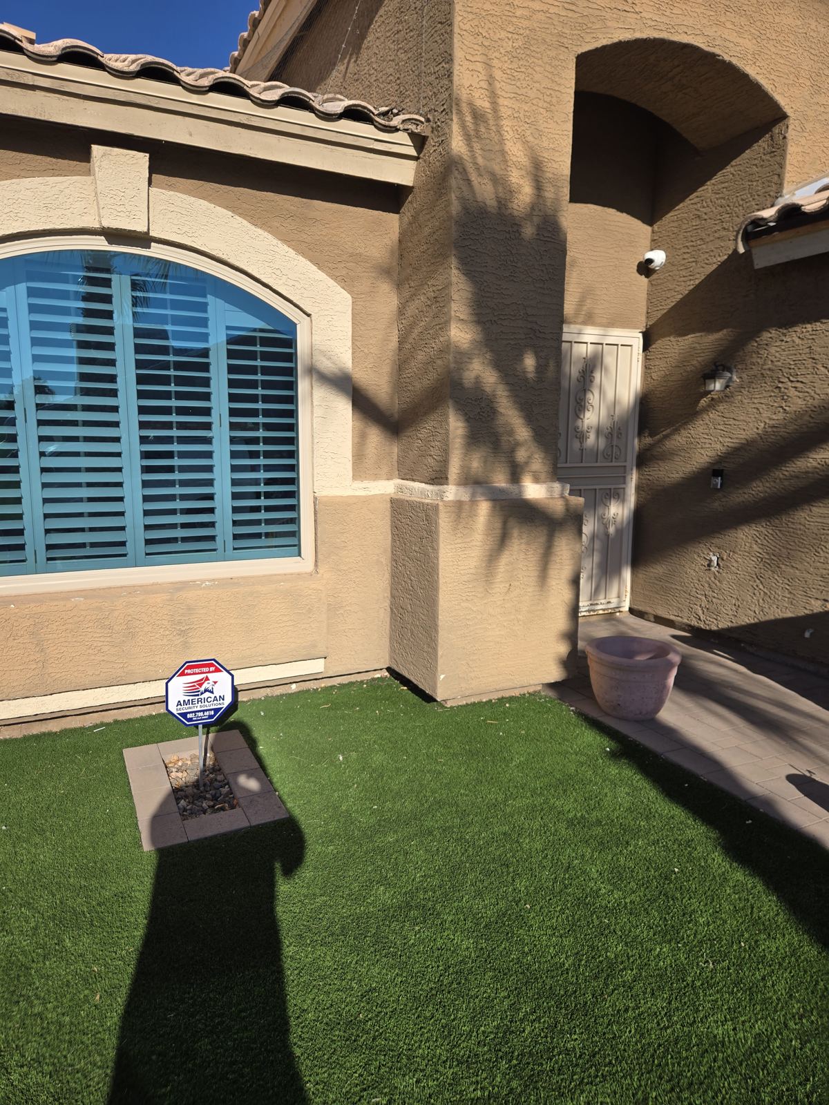 Stucco home protected by a security camera and an American Security Solutions yard sign