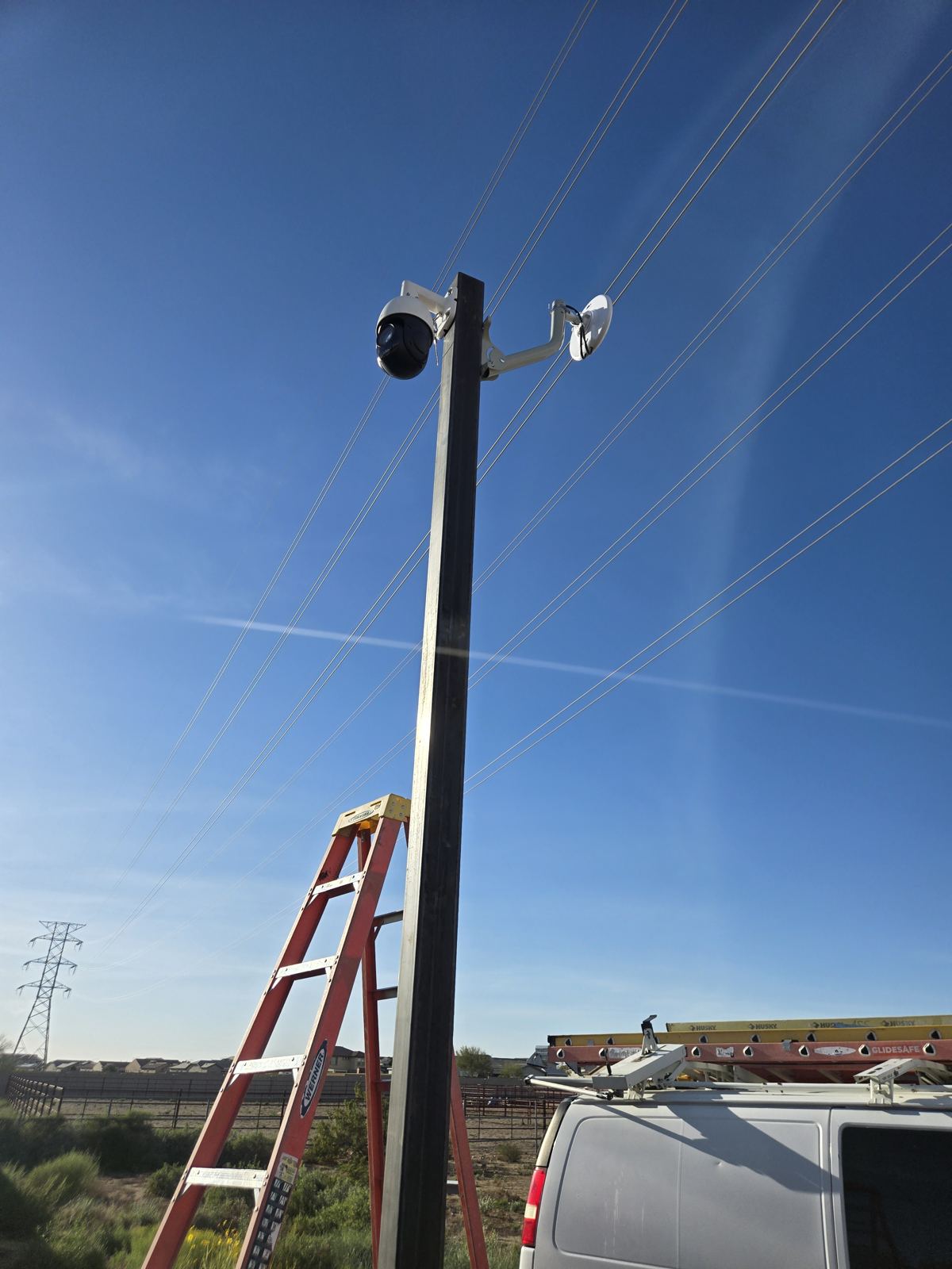 Camera pole beside a ladder and a work van on a sunny day