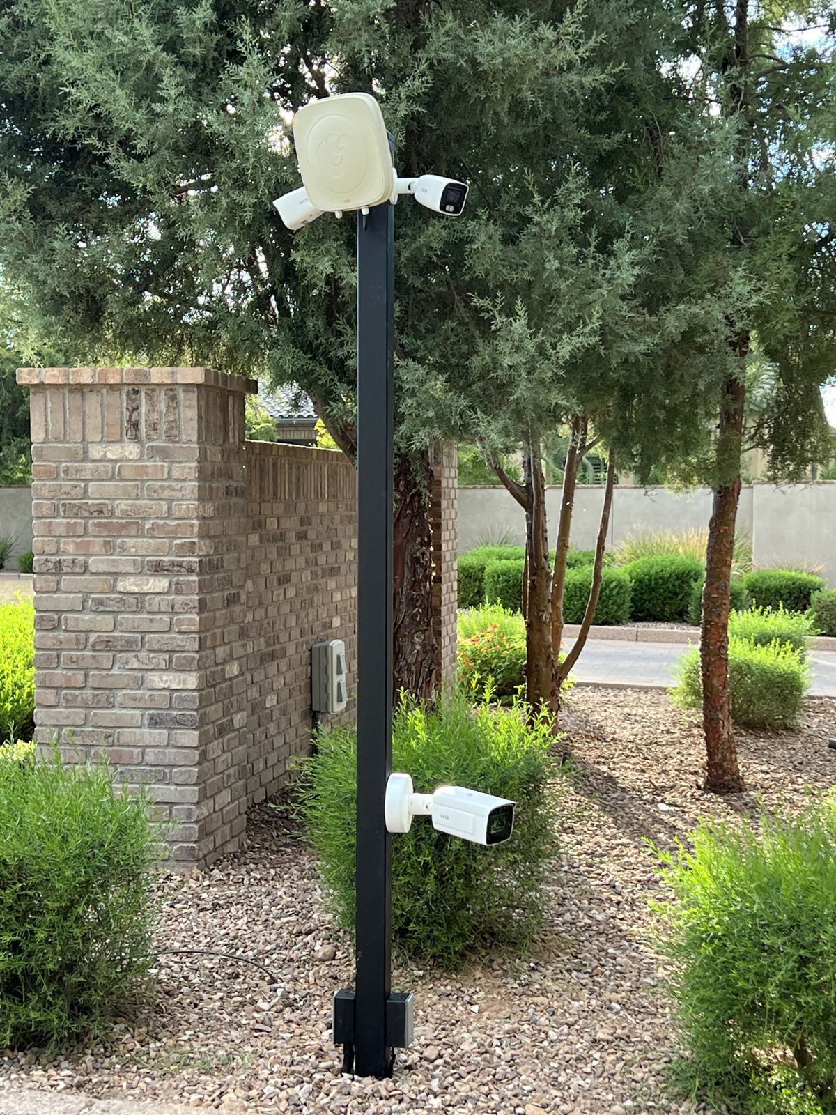 Security camera on a black pole at a landscaped community entrance
