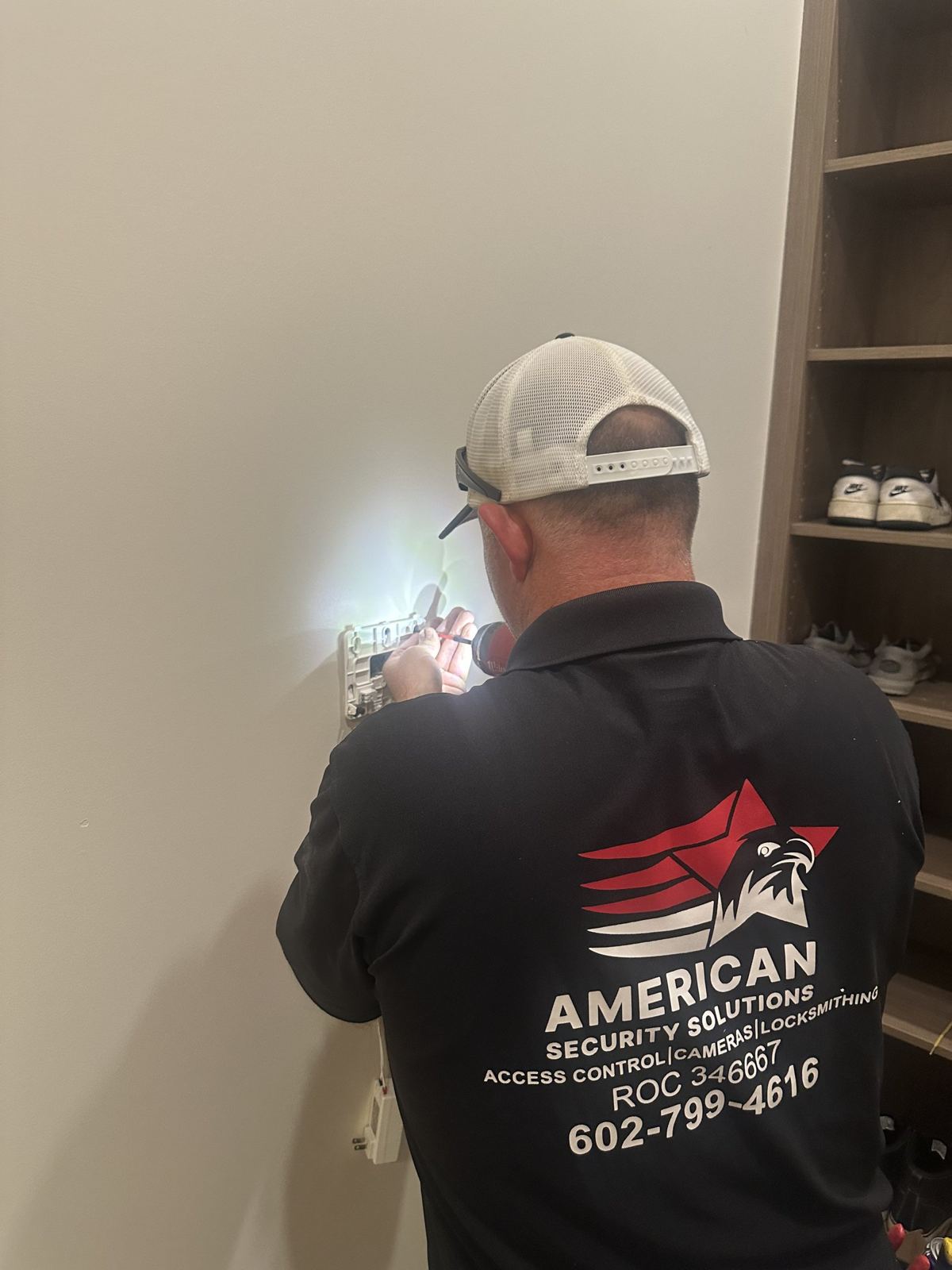 Technician in an American Security Solutions shirt installing a device inside a home