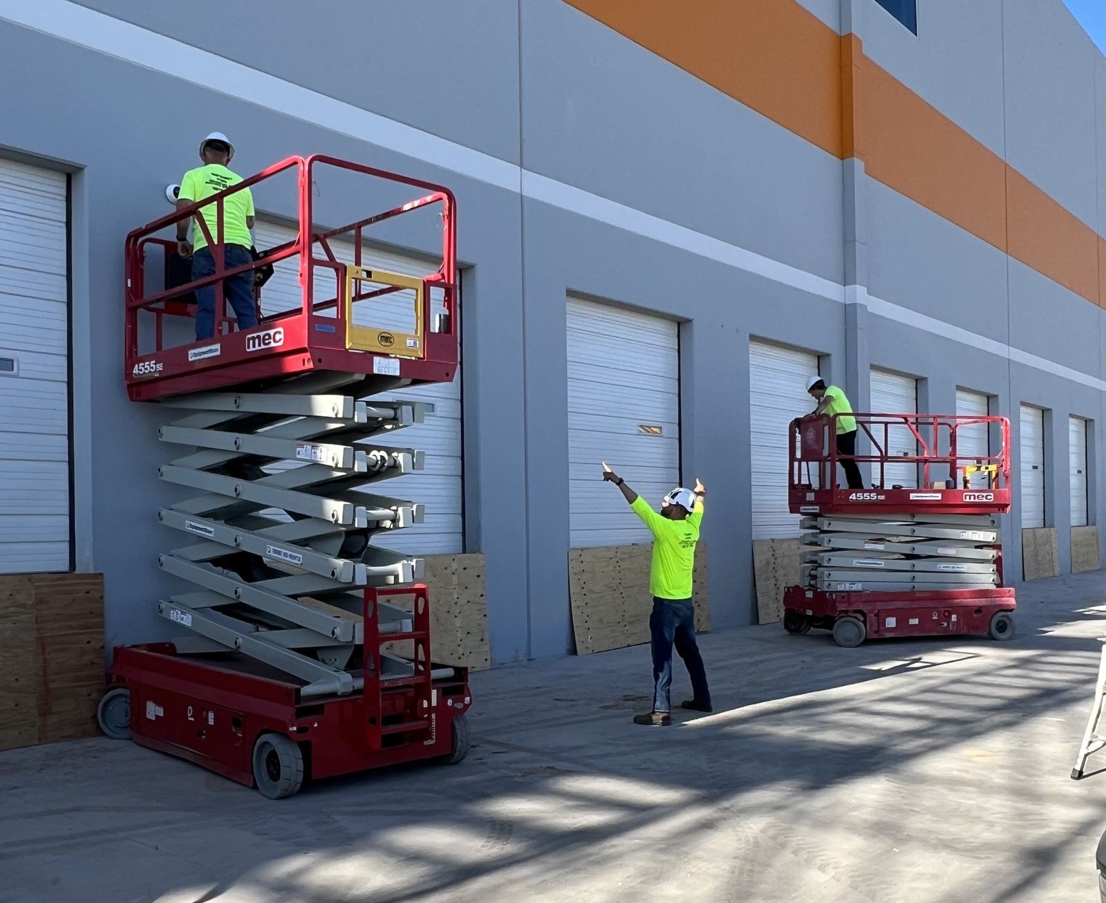 Two technicians on scissor lifts installing cameras along a warehouse wall